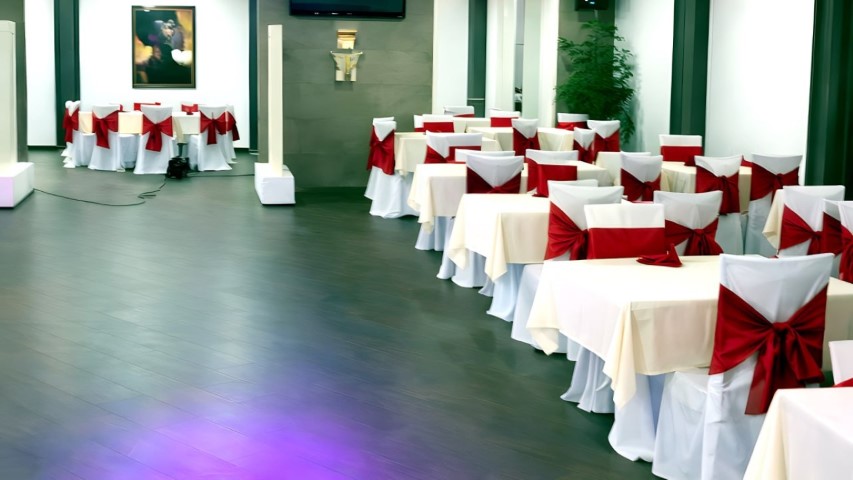 Sala de eventos del Hotel Ruta Romana con sillas blancas y lazos rojos