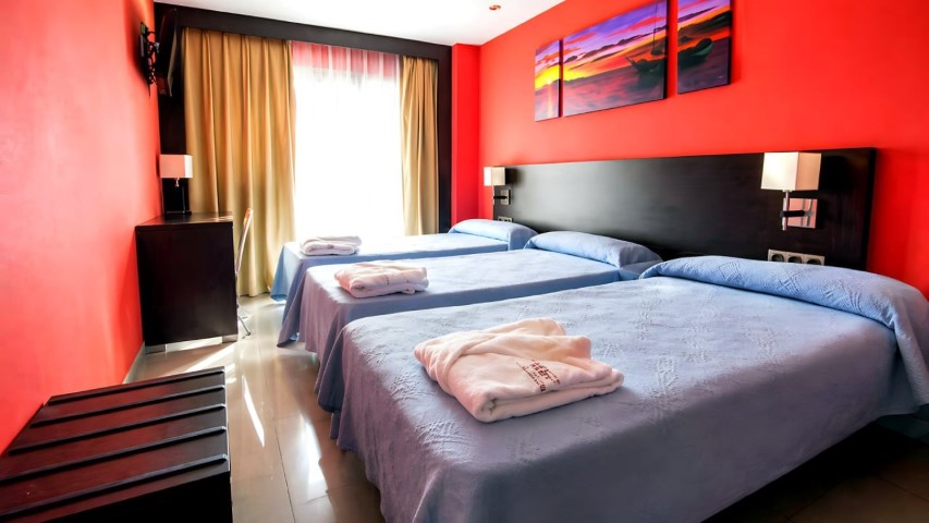 Habitación triple con colchas azules y toallas con logo