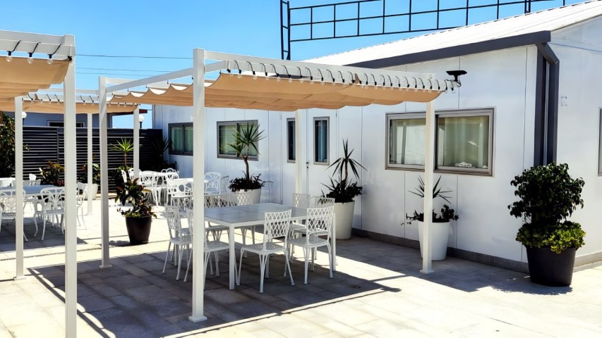 Terraza interior con pérgolas blancas y mesas de metal