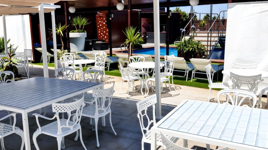 Terraza con mesas blancas en primer plano y piscina al fondo